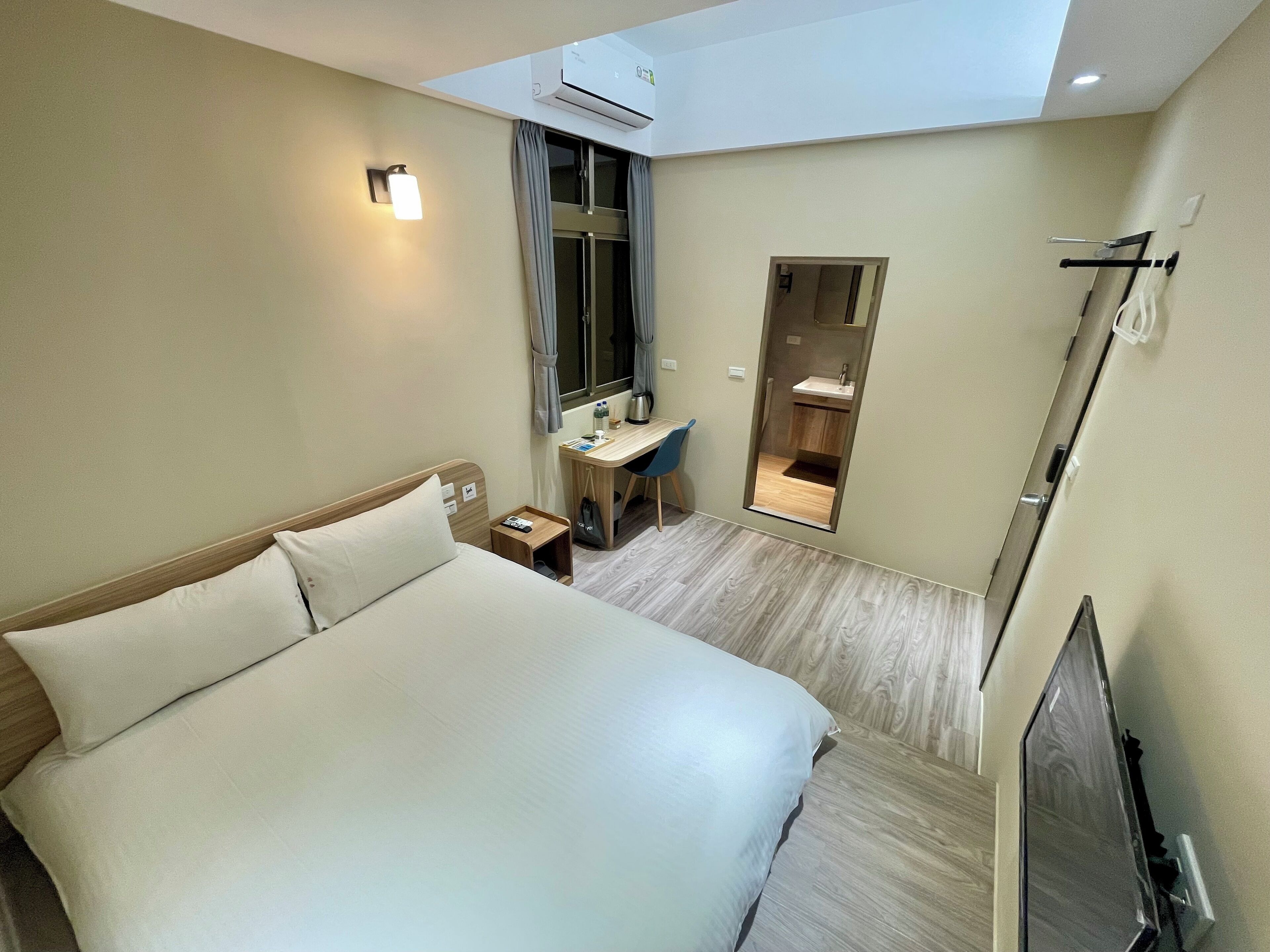 A hotel room with a large bed, a desk with a chair, a small bathroom, and a TV.