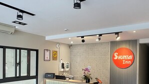 A reception desk with a Shuntai Inn sign, a reception area with a counter, a plant, and a wall-mounted security camera. - Shuntai Inn (Shoufeng)