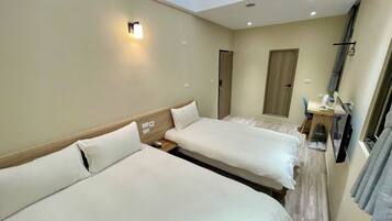 A hotel room with two beds, a desk with a chair, a small table, a mirror, and a window with curtains.