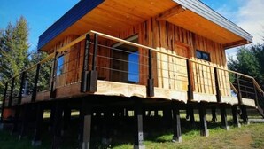 Una cabaña de madera con balcón, elevada sobre pilotes y rodeada de árboles.
