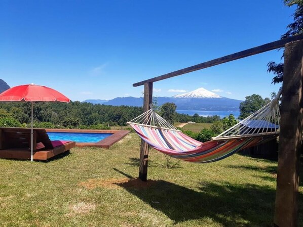 A hammock, a red umbrella, and a pool in a backyard with a mountain view. - Karibuni - Familiar Lodging & Private Spa (Villarrica)