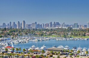 A marina with numerous boats docked, a city skyline in the background, and a clear blue sky.