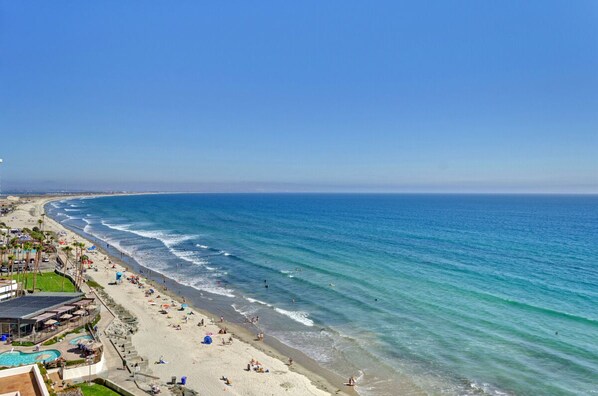 A beach with a pool, umbrellas, and a clear blue sky.