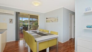 Un petit coin repas avec une table et des chaises, une vue sur une terrasse extérieure par le biais d’une porte, et une étagère murale sur laquelle est posée une voiture jouet.