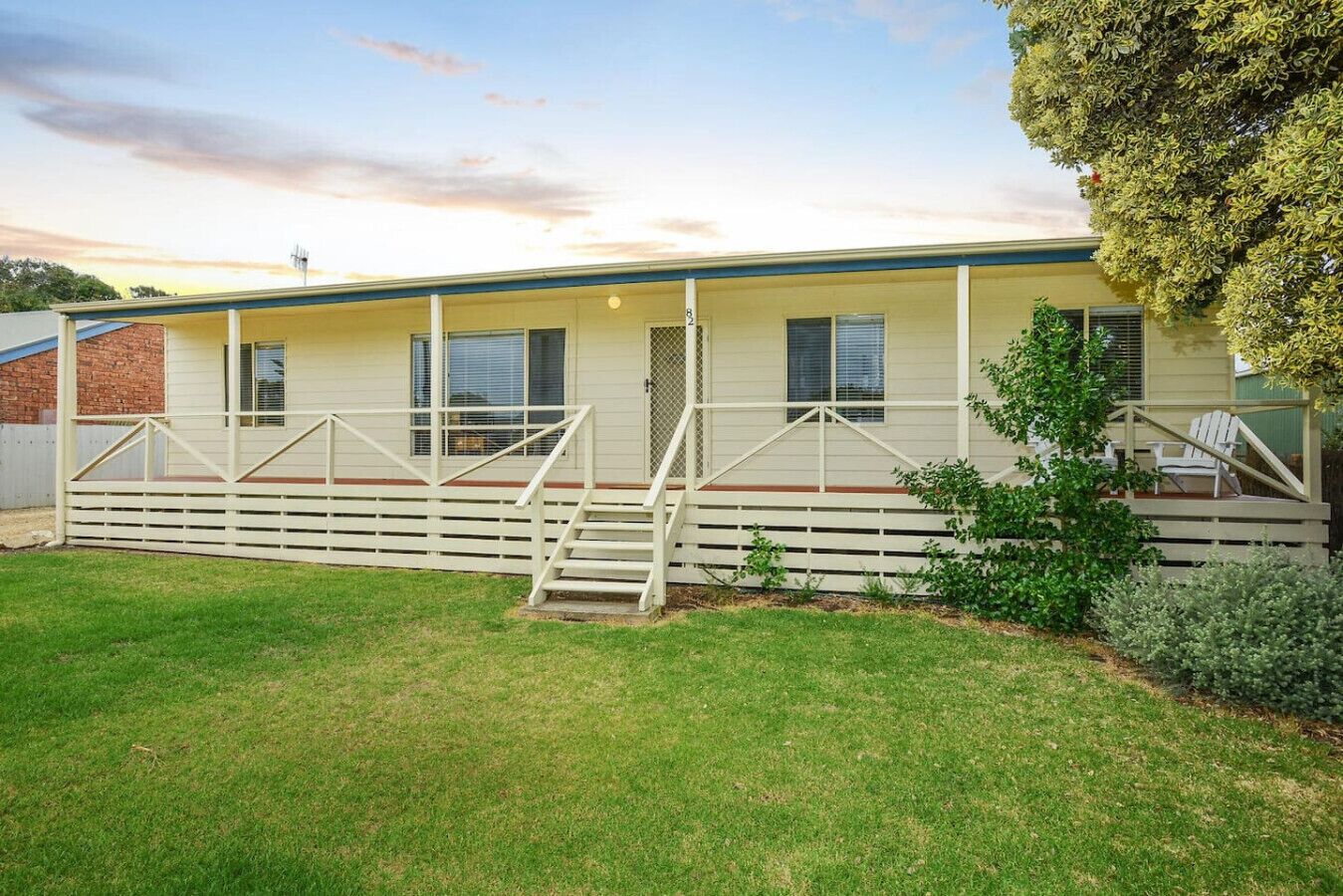 A single-story mobile home with a covered porch, a small front yard, and a tree to the right.