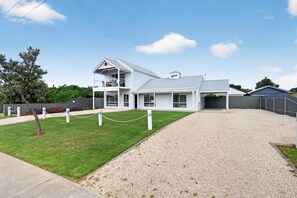 A two-story house with a covered porch, a fenced yard, and a gravel driveway.