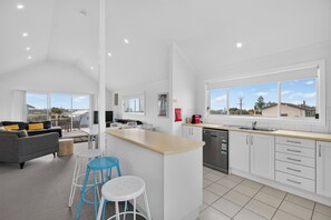 A modern kitchen with white cabinets, a stainless steel dishwasher, and a large window.