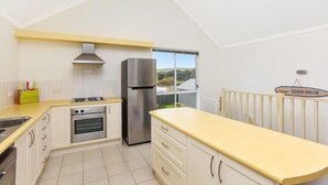 Eine moderne Küche mit Edelstahl-Kühlschrank, Backofen und Gasherd. Eine gelbe Arbeitsplatte und weiße Schränke sorgen für einen hellen Look. Ein Fenster bietet Blick ins Freie.