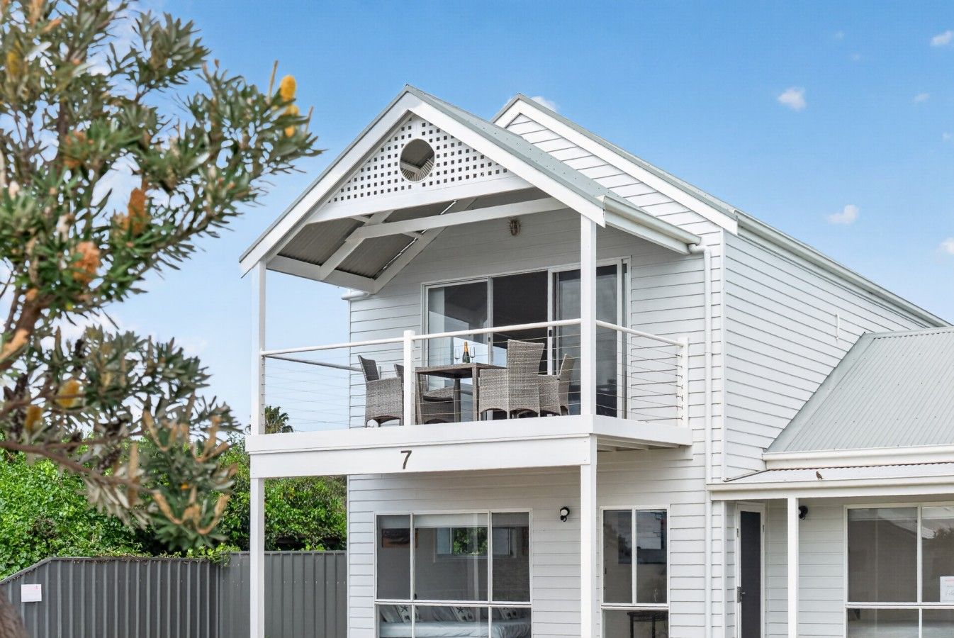 A two-story house with a balcony, a number '7' on the front, and a fenced yard.