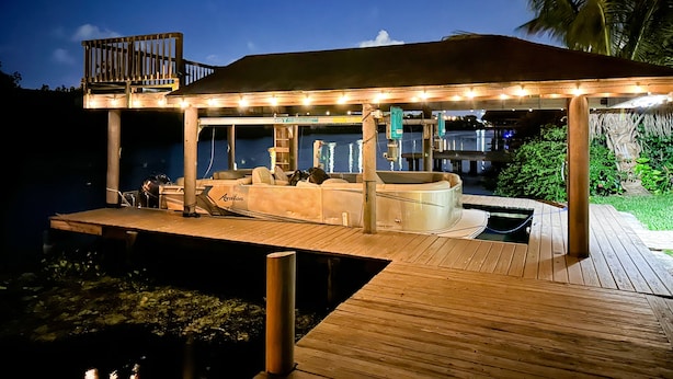 Una terraza de madera con jacuzzi y zona de estar, con vista a un cuerpo de agua.