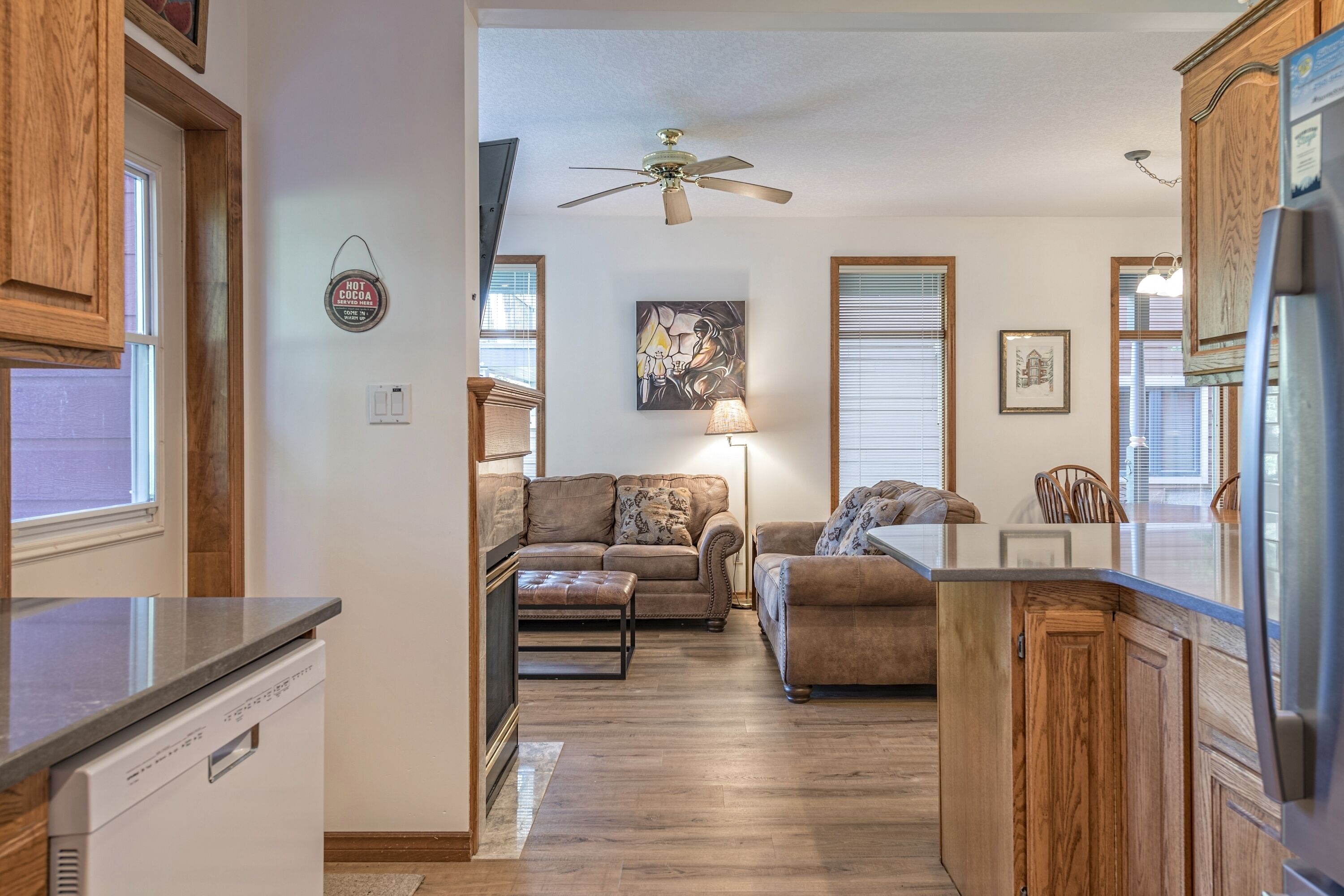 A kitchen with wooden cabinets, a dishwasher, and a ceiling fan. There is a living area with a sofa and a coffee table.