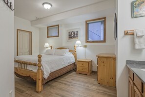 Ein Schlafzimmer mit einem Holzbett, Nachttischen, einem Beistelltisch, einem Holzschrank und einem Fenster mit Jalousien.