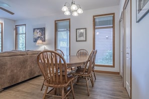 Enjoy meals in this dining area with a wooden table and six chairs, surrounded by large windows and a ceiling fan.