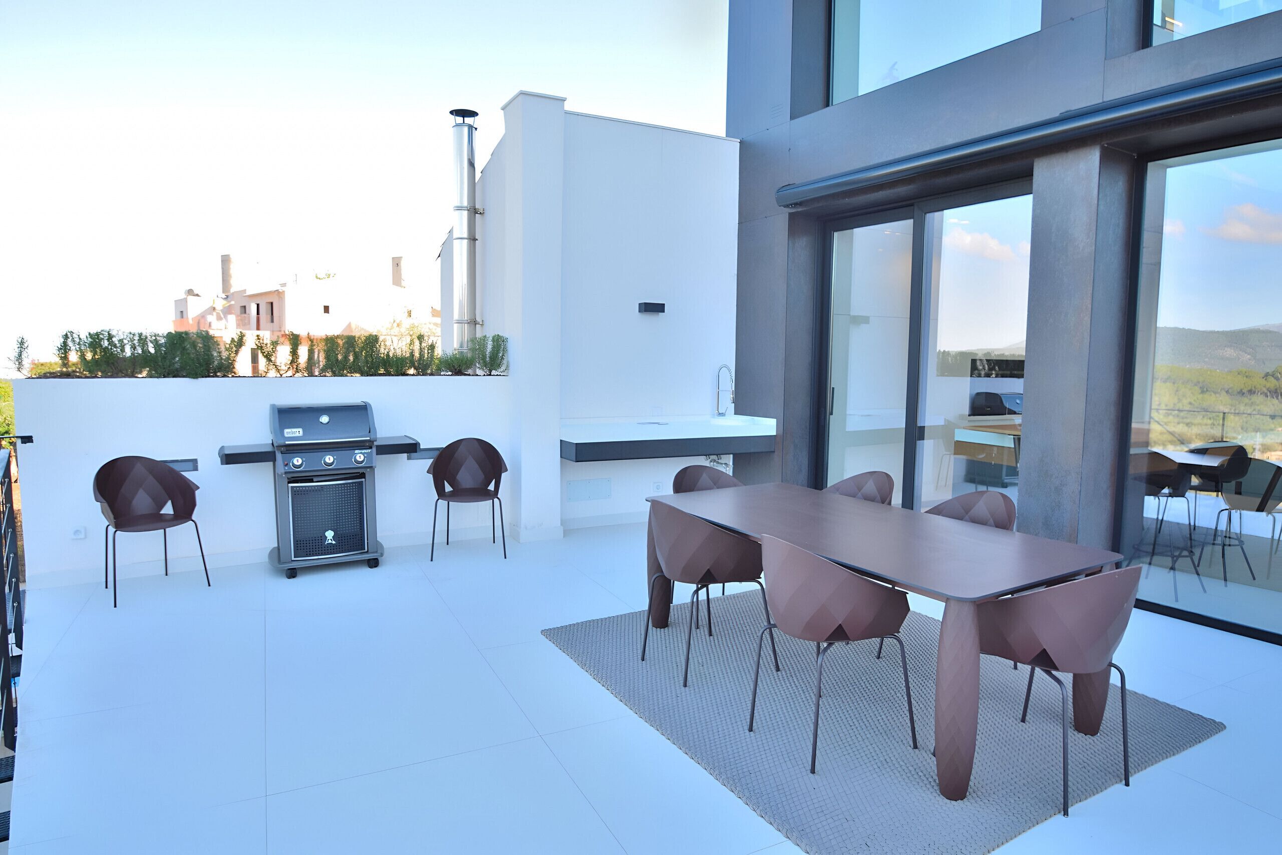 A modern outdoor patio with a dining table and chairs, a grill, and a view of the cityscape.