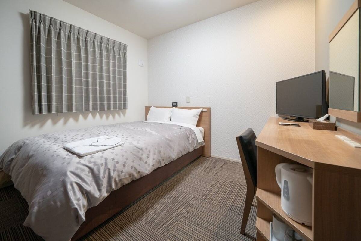 Ein Hotelzimmer mit einem Bett, einem Schreibtisch mit Computer, einem Sessel und einem Fernseher.