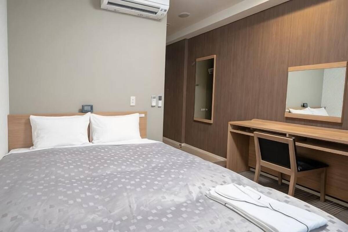 Ein Hotelzimmer mit einem Bett, einem Schreibtisch, einem Spiegel und einer Klimaanlage.