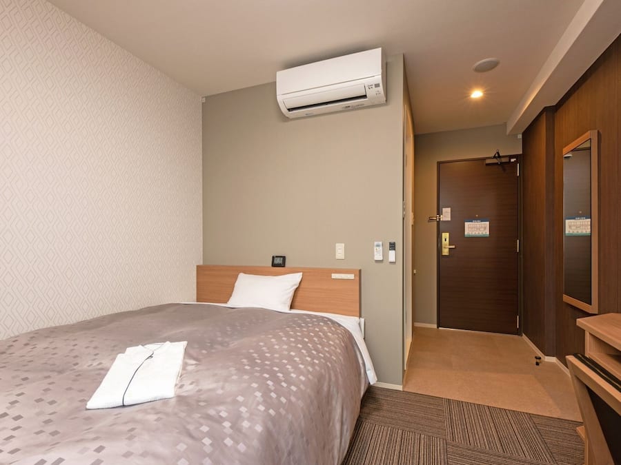 A hotel room with a bed, an air conditioner, a wooden wardrobe, and a door with a sign.