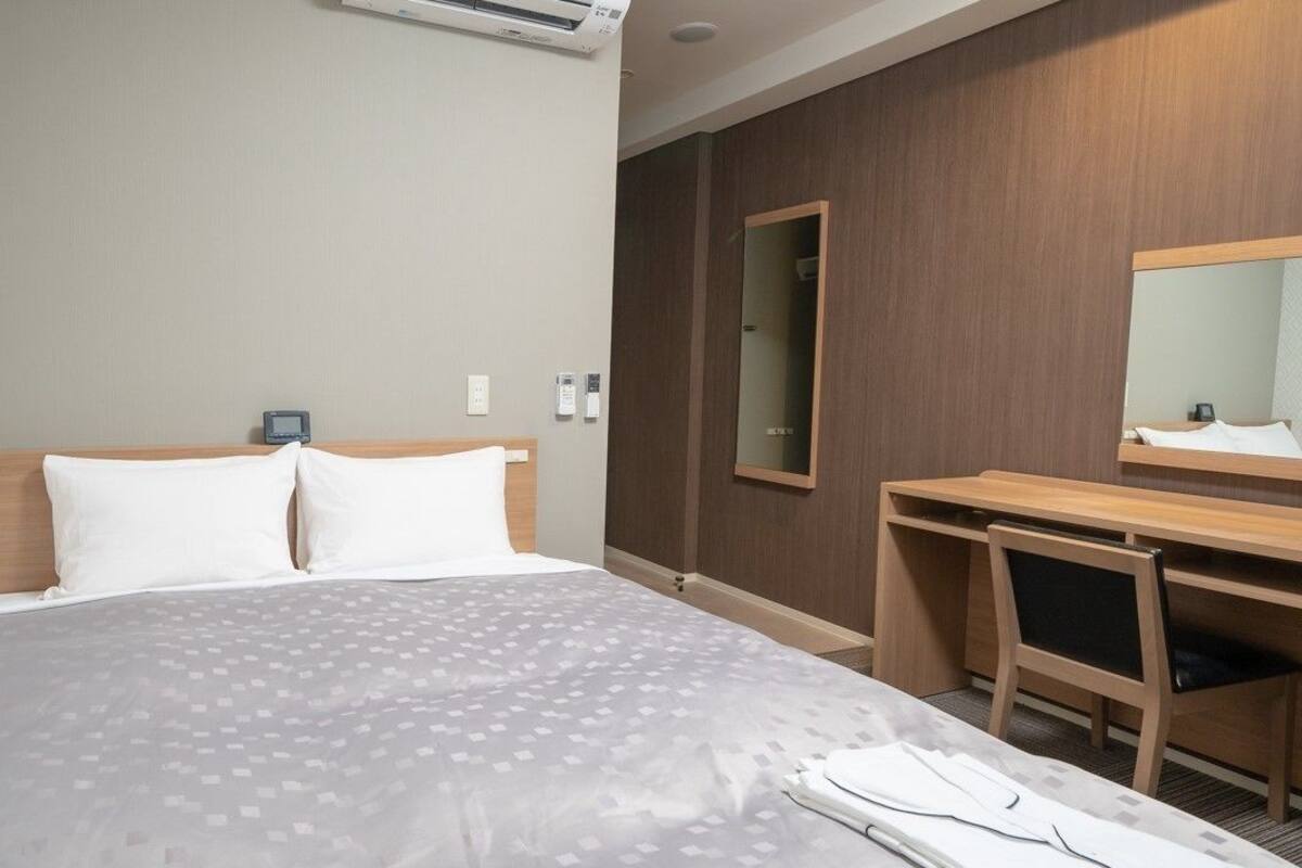 Ein Hotelzimmer mit einem Bett, einem Schreibtisch, einem Sessel und einem Spiegel sowie einer Klimaanlage.