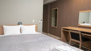 Una camera d'albergo con un letto, una scrivania, una sedia, uno specchio e un condizionatore d'aria.