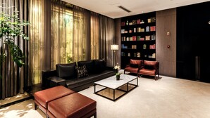 Un salon moderne avec un canapé en cuir noir, un fauteuil en cuir rouge, une table basse en verre et une bibliothèque remplie de livres.