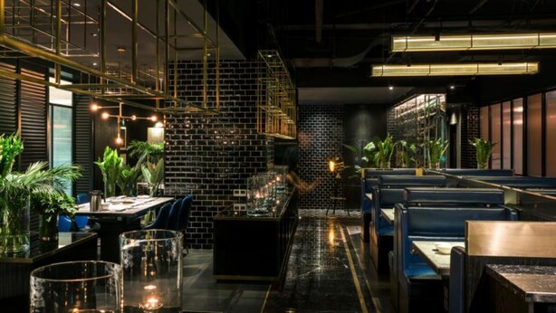 Un intérieur de restaurant moderne avec des murs en briques noires, des rampes en métal et des sièges bleus.