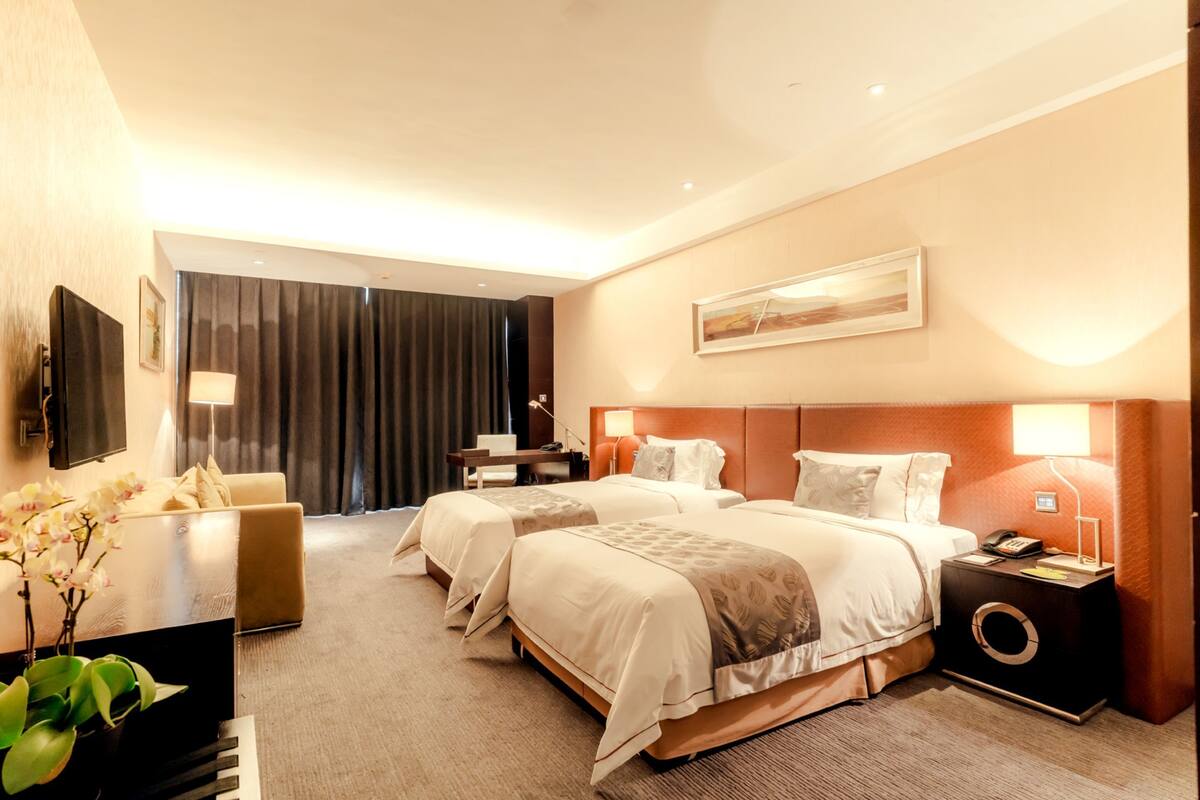Une chambre d’hôtel avec deux lits, un bureau, une chaise, une télévision et un tableau au mur.