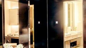 Une chambre d’hôtel moderne dotée d’un grand miroir, d’une coiffeuse avec un lavabo et d’une salle de bain séparée.