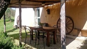 A rustic outdoor dining area with a wooden table and chairs, a thatched roof, and a large wheel visible in the background. - Groundfloor apt with al fresco dining, shared pool & wi-fi on awarded winery. (Bucine)