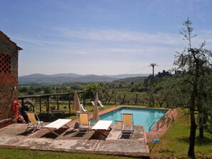 A pool area with lounge chairs and umbrellas, surrounded by a brick wall and a view of distant mountains. - Groundfloor apt with al fresco dining, shared pool & wi-fi on awarded winery. (Bucine)