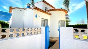 A white building with a blue door and a blue gate, featuring a small window and a blue roof.