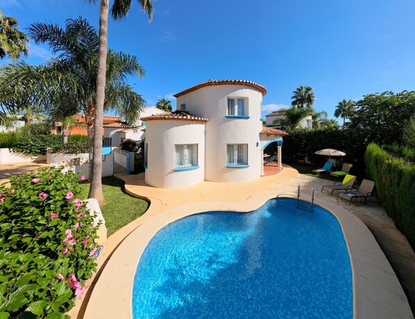 A modern villa with a swimming pool, surrounded by lush greenery and palm trees.