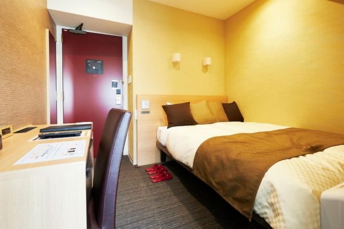 Una habitación de hotel con cama, escritorio y silla, y una puerta.