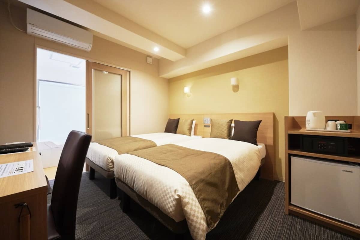 Habitación de hotel con dos camas, un escritorio, una silla, un refrigerador miniatura y un microondas.