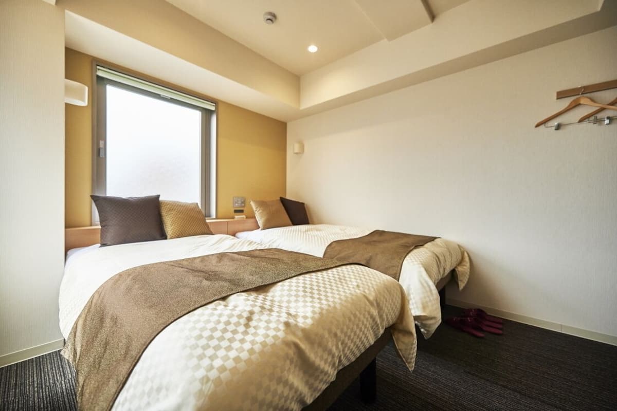 Habitación de hotel con dos camas, un ventanal grande y un perchero.