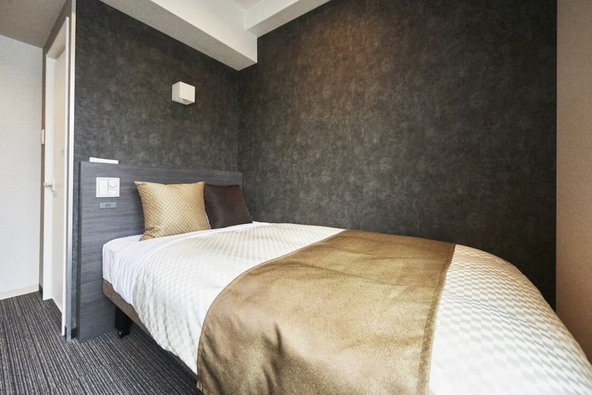 Habitación de hotel con cama, cabecero, lámpara de pared y suelo cubierto de alfombra.