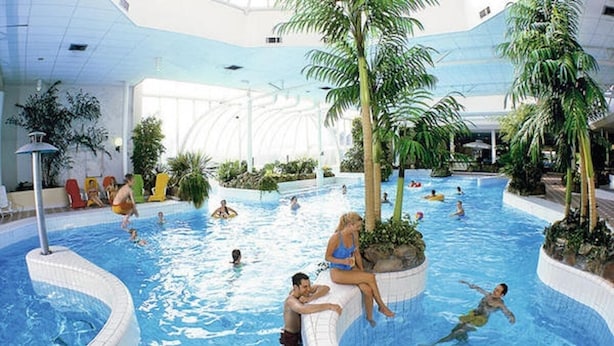 Une piscine intérieure dotée de plusieurs couloirs, de palmiers et de chaises longues.