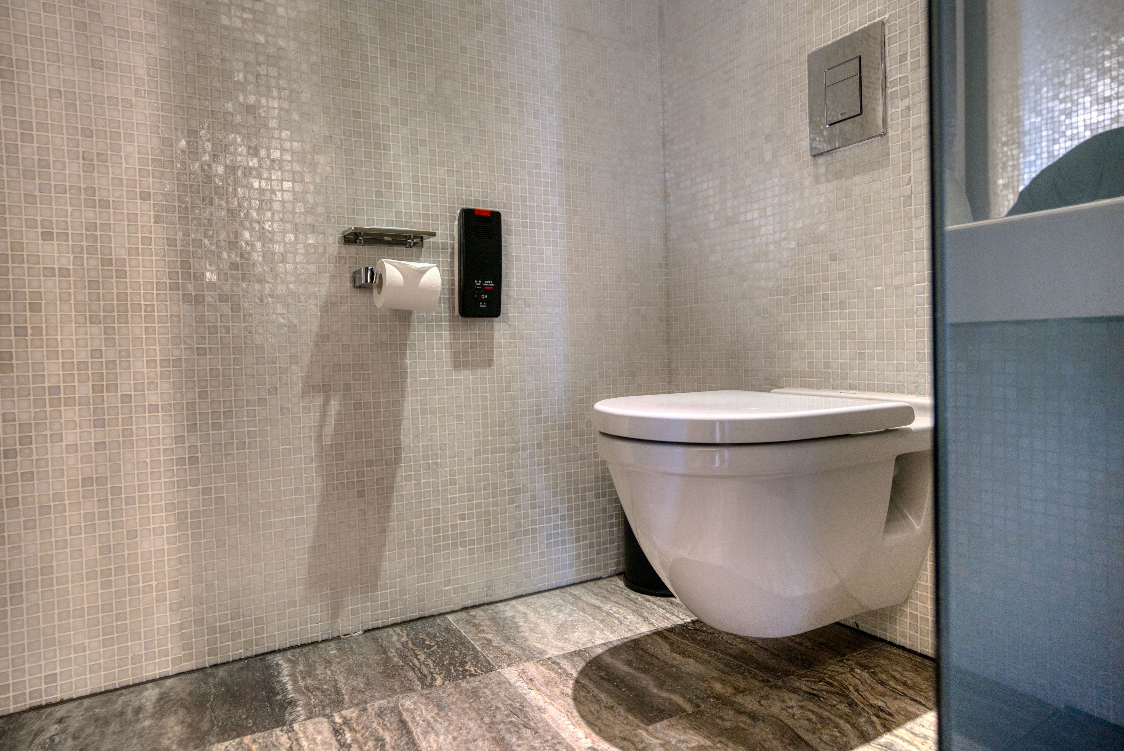 A modern bathroom with a toilet, a paper towel dispenser, and a flush button.