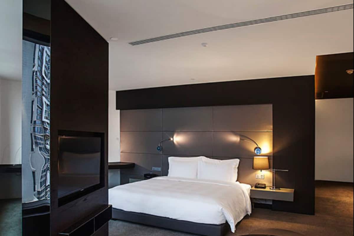 A modern hotel room with a large bed, a TV, a desk, and a coffee table.