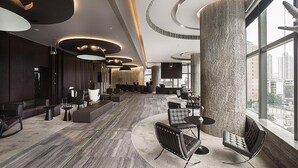 Eine geräumige Lobby mit moderner Möblierung, einer großen Säule und Blick auf die Stadt durch große Fenster.