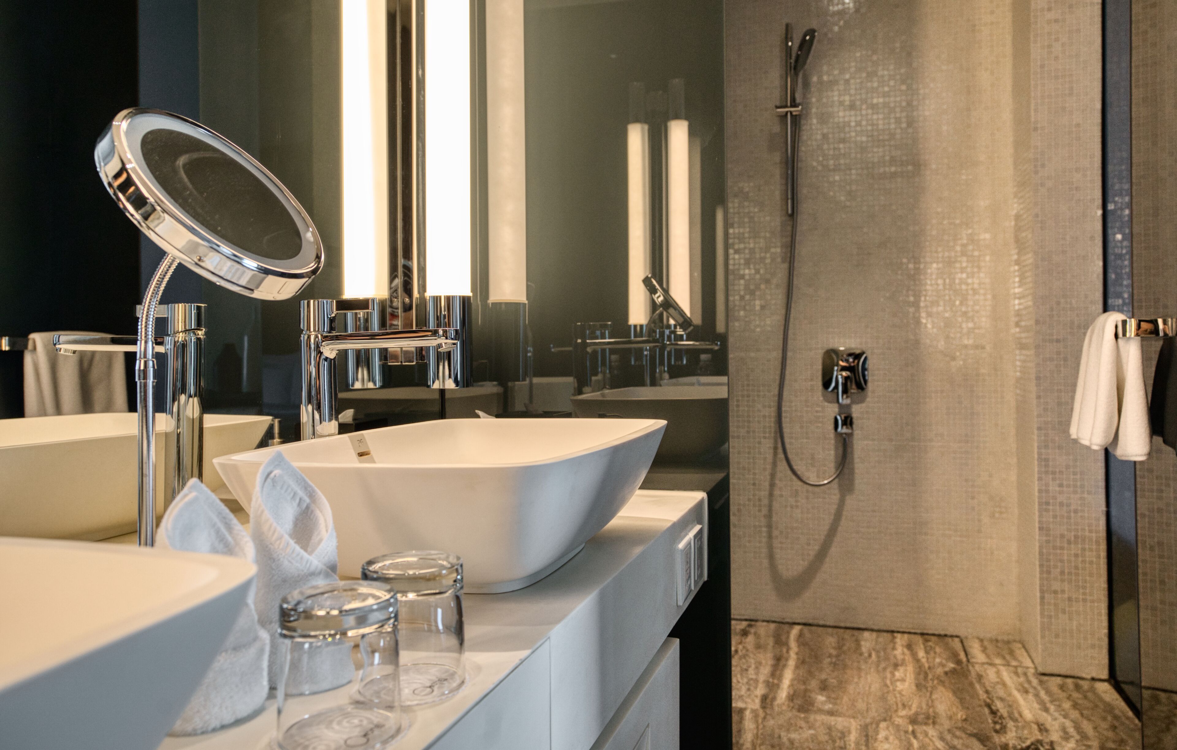 A modern bathroom with two sinks, a mirror, a shower, and a towel rack.