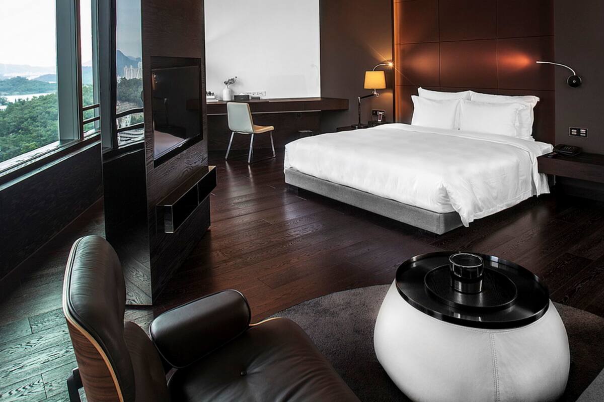 A modern hotel room with a large bed, a desk, a chair, a TV, and a view of the outdoors.