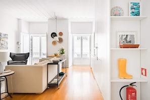 A modern living room with a sofa, a small table, and a cart with items. There are two doors leading to another room.