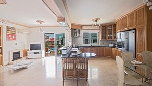 A spacious kitchen with wooden cabinets, a central island, and a dining area with chairs. - Luxury 5BDR Villa with Private pool, and wheelchair accessible flat (Paralimni)