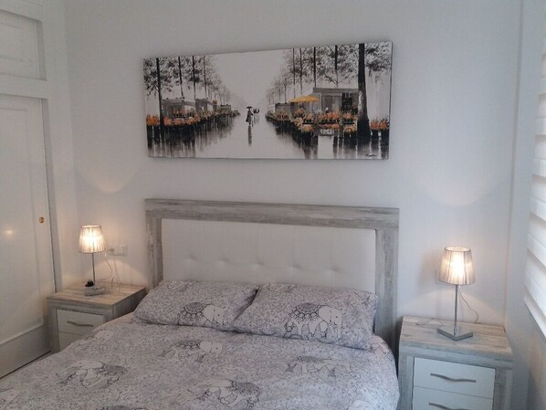 A bedroom with a bed, two bedside tables, a headboard, and a wall-mounted painting. - Perfectly located, refurbished apartment in a gated complex with pool and garden (Torrevieja)