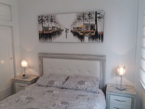 Une chambre à coucher comprenant un lit, deux tables de chevet, une tête de lit et un tableau accroché au mur.