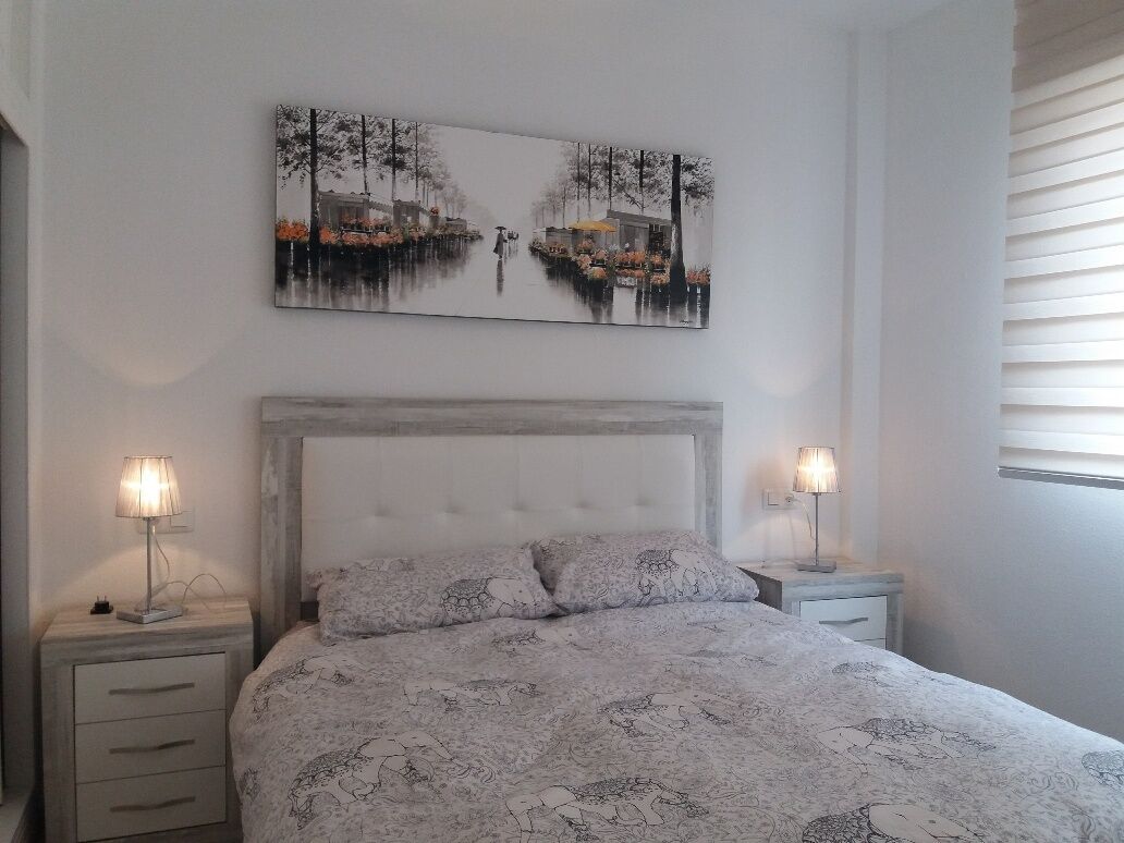 A bedroom with a bed, two bedside tables, a headboard, and a wall-mounted painting.
