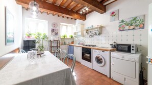 Eine Küche mit Esstisch, Waschmaschine, Mikrowelle und Holzbalkendecke.