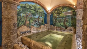 Vasca idromassaggio con pareti in pietra e un affresco raffigurante una scena di bosco.