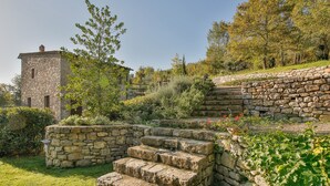 Una scala in pietra conduce a un edificio con un muro di pietra e un'area verde con piante e alberi.