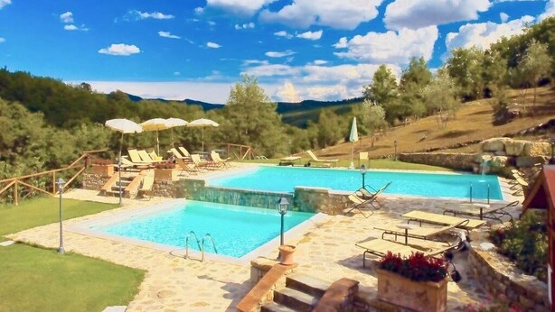Area piscina con due piscine, lettini, ombrelloni e un vialetto in pietra.